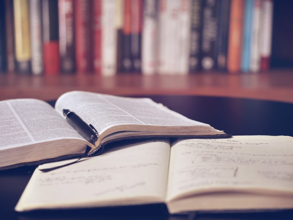 shelf of books in background with two open books in foreground.